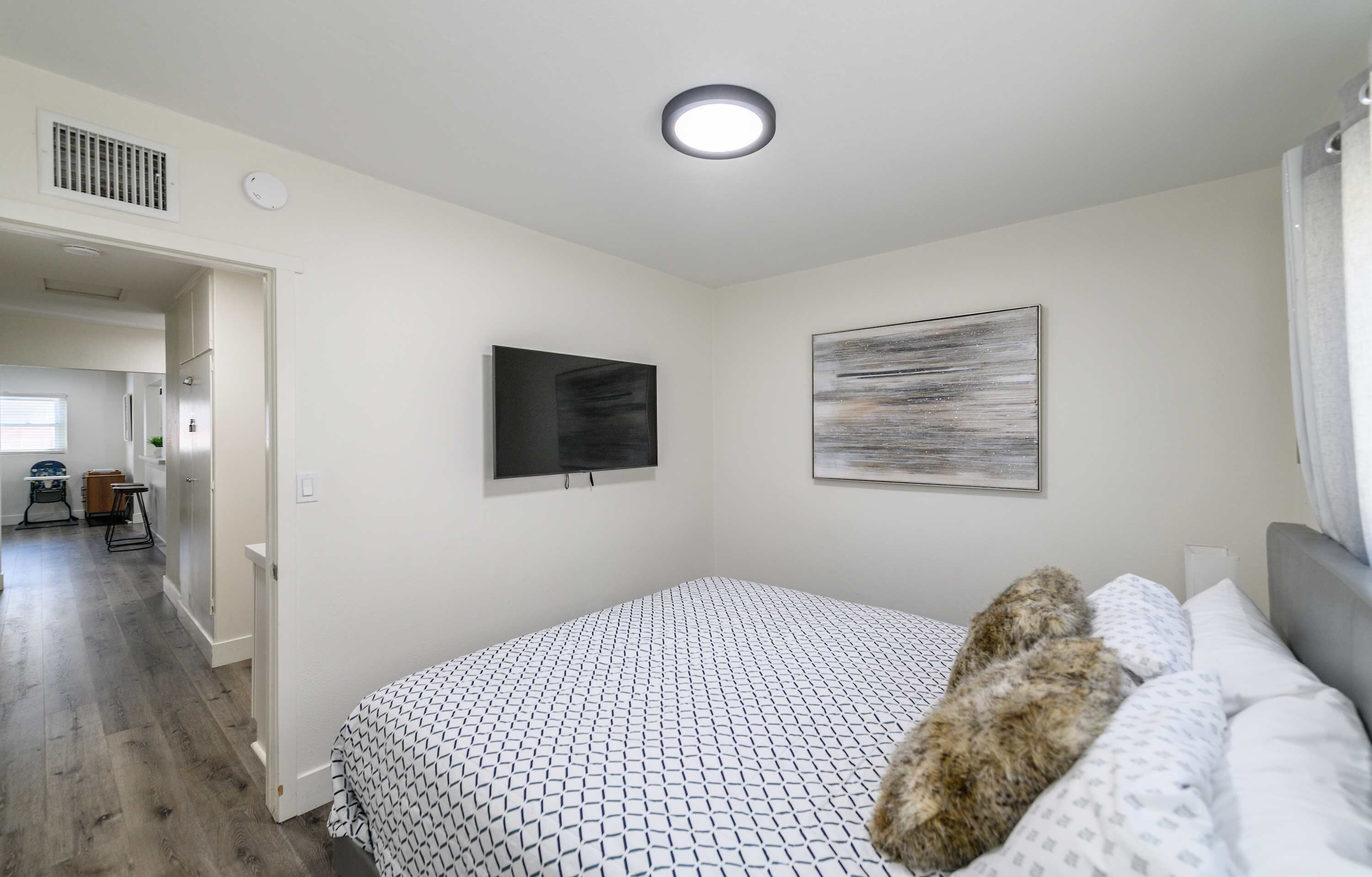 A bedroom with a bed, a television, a painting, and a door leading to a bathroom.