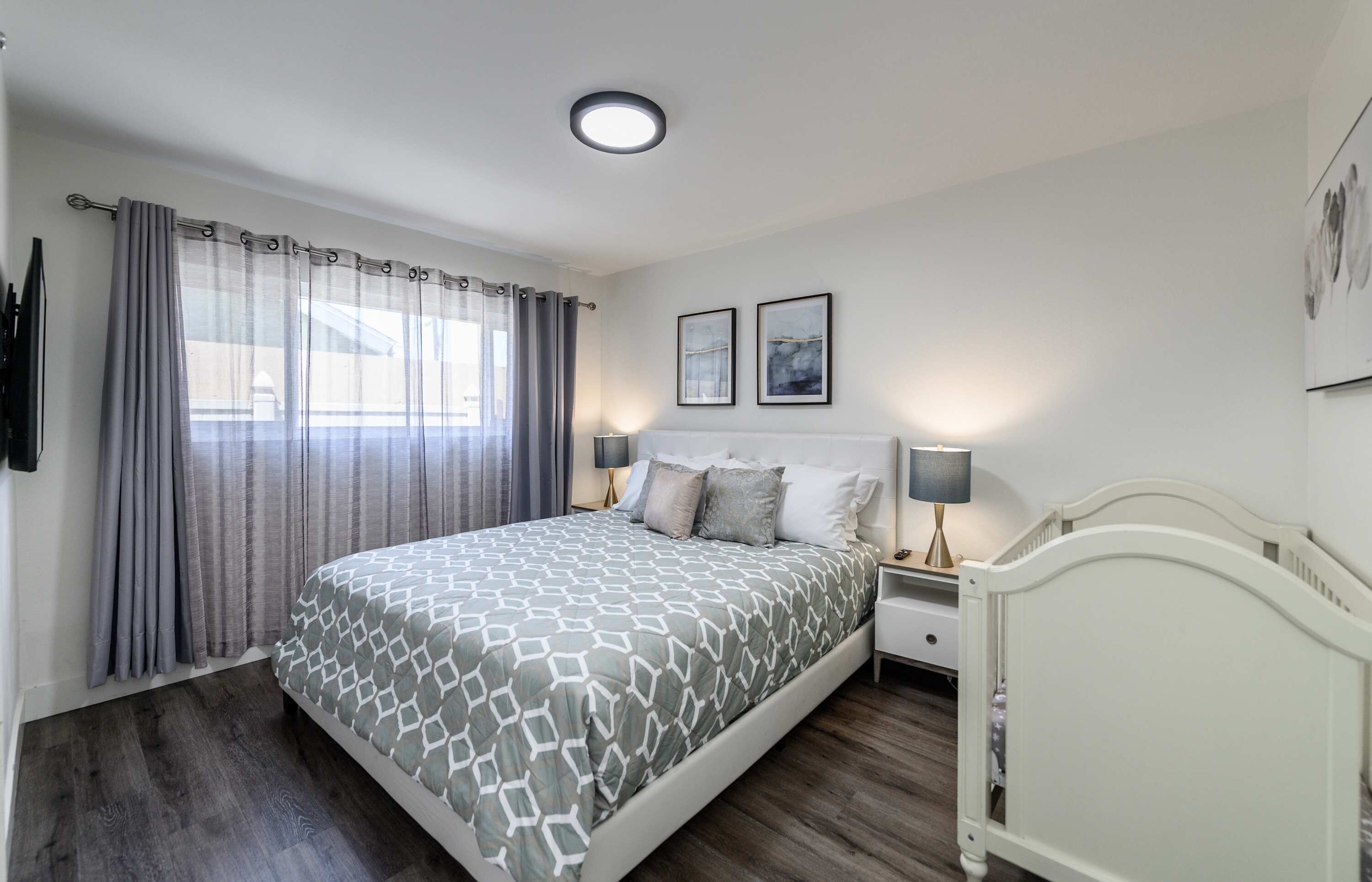 A bedroom with a bed, two bedside tables, a nightstand, a ceiling light, and two framed pictures on the wall.