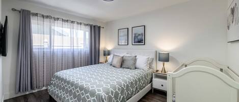 A bedroom with a bed, two bedside tables, a nightstand, a ceiling light, and two framed pictures on the wall.