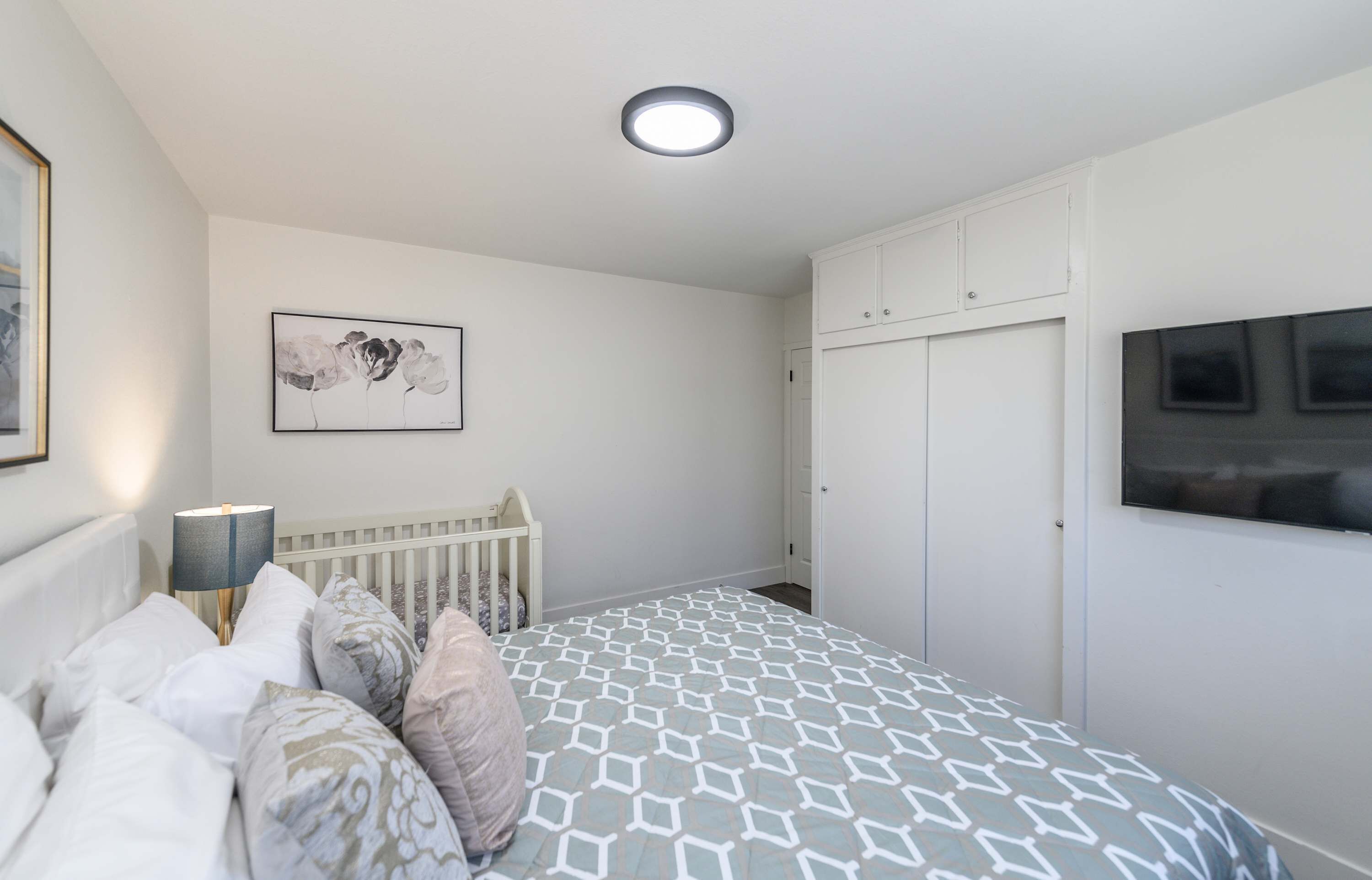 A bedroom with a bed, a crib, a wardrobe, and a painting on the wall.