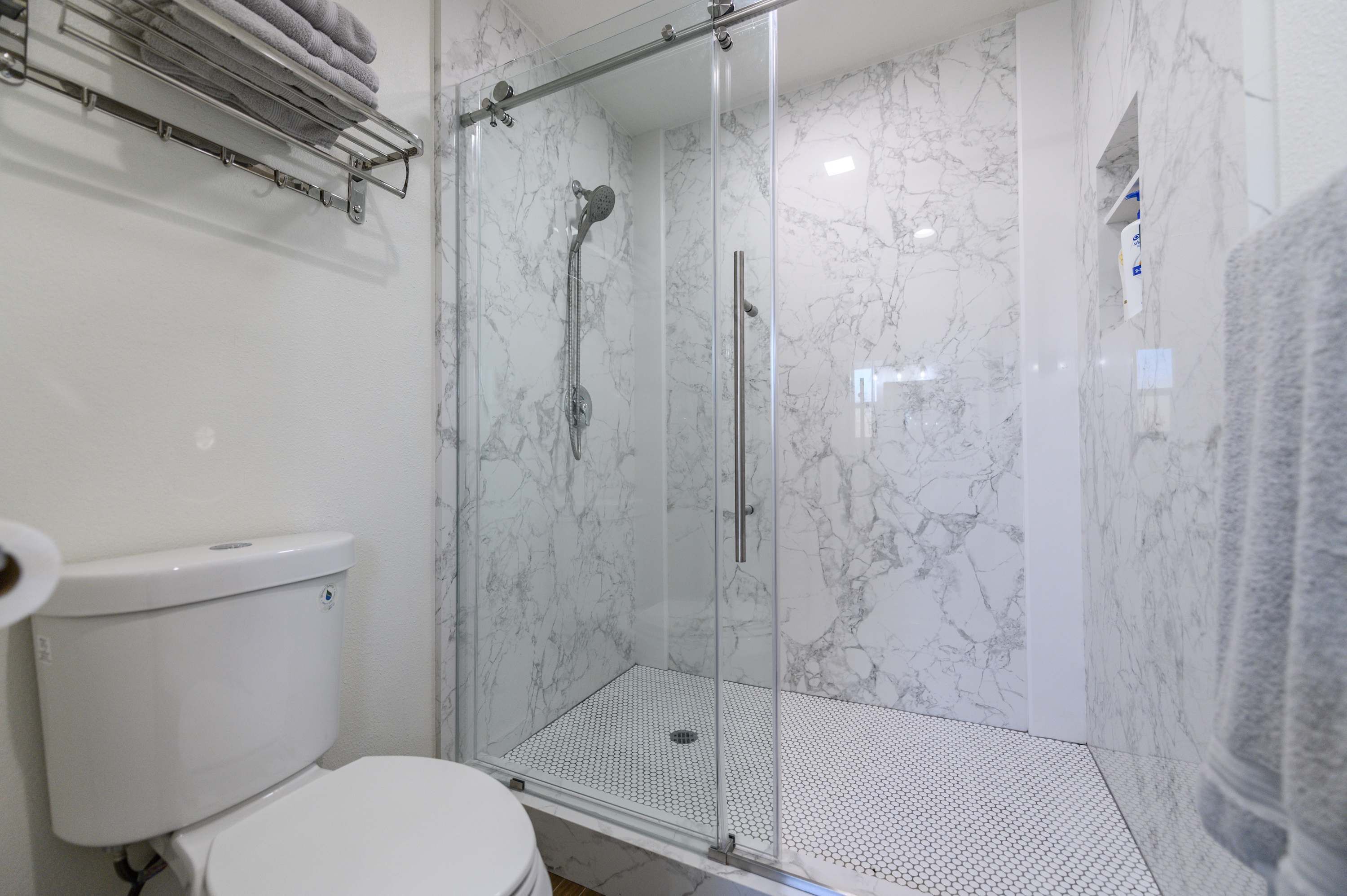 Ein Badezimmer mit einer gläsernen Duschkabine, Toilette und Handtuchhalter.