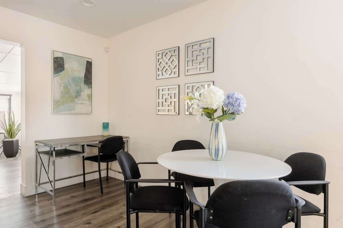 A modern room with a round table, four chairs, a vase with flowers, and abstract wall art.