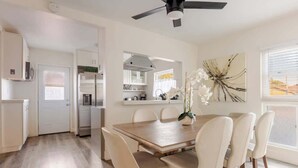 A modern kitchen with white cabinets, a dining area with a wooden table and chairs, and a ceiling fan. - Disneyland/Knott's, 5BR 4BA, No Tax, Large Parking (Fullerton)