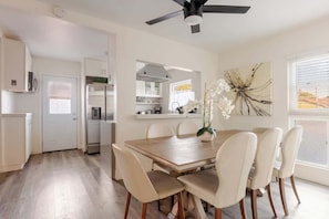 Una cocina moderna con armarios blancos, un comedor con mesa y sillas de madera, y un ventilador de techo.