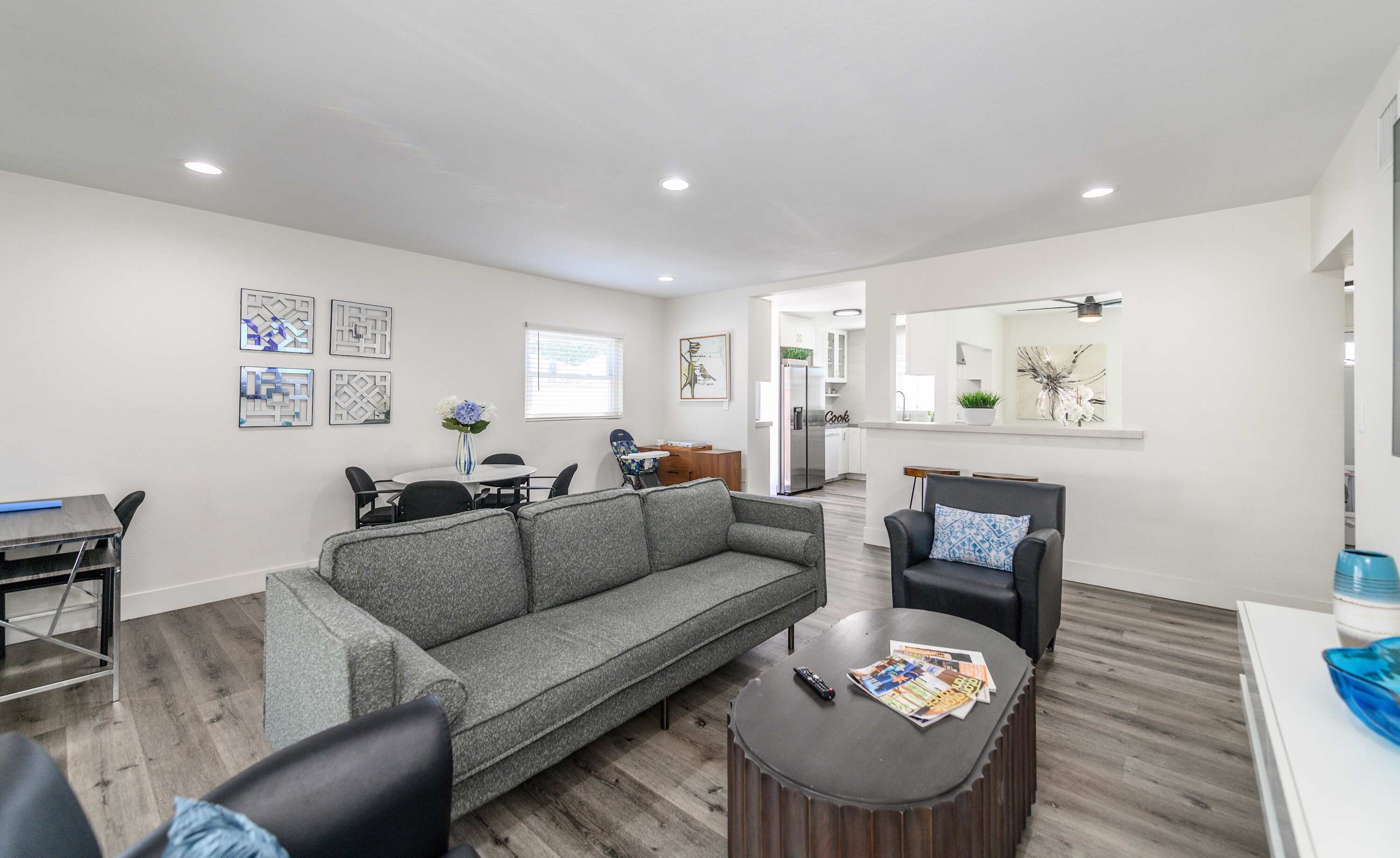 A modern living room with a grey sofa, a round coffee table, and a dining area with a white table and chairs.