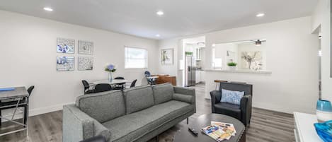 A modern living room with a grey sofa, a round coffee table, and a dining area with a white table and chairs.