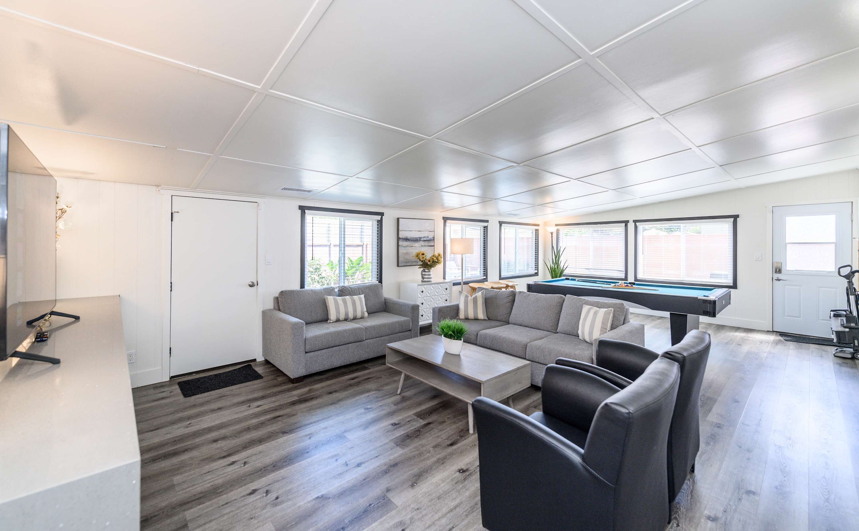 A modern living room with a grey sectional sofa, a coffee table, and a pool table.