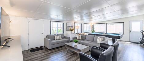 A modern living room with a grey sectional sofa, a coffee table, and a pool table.