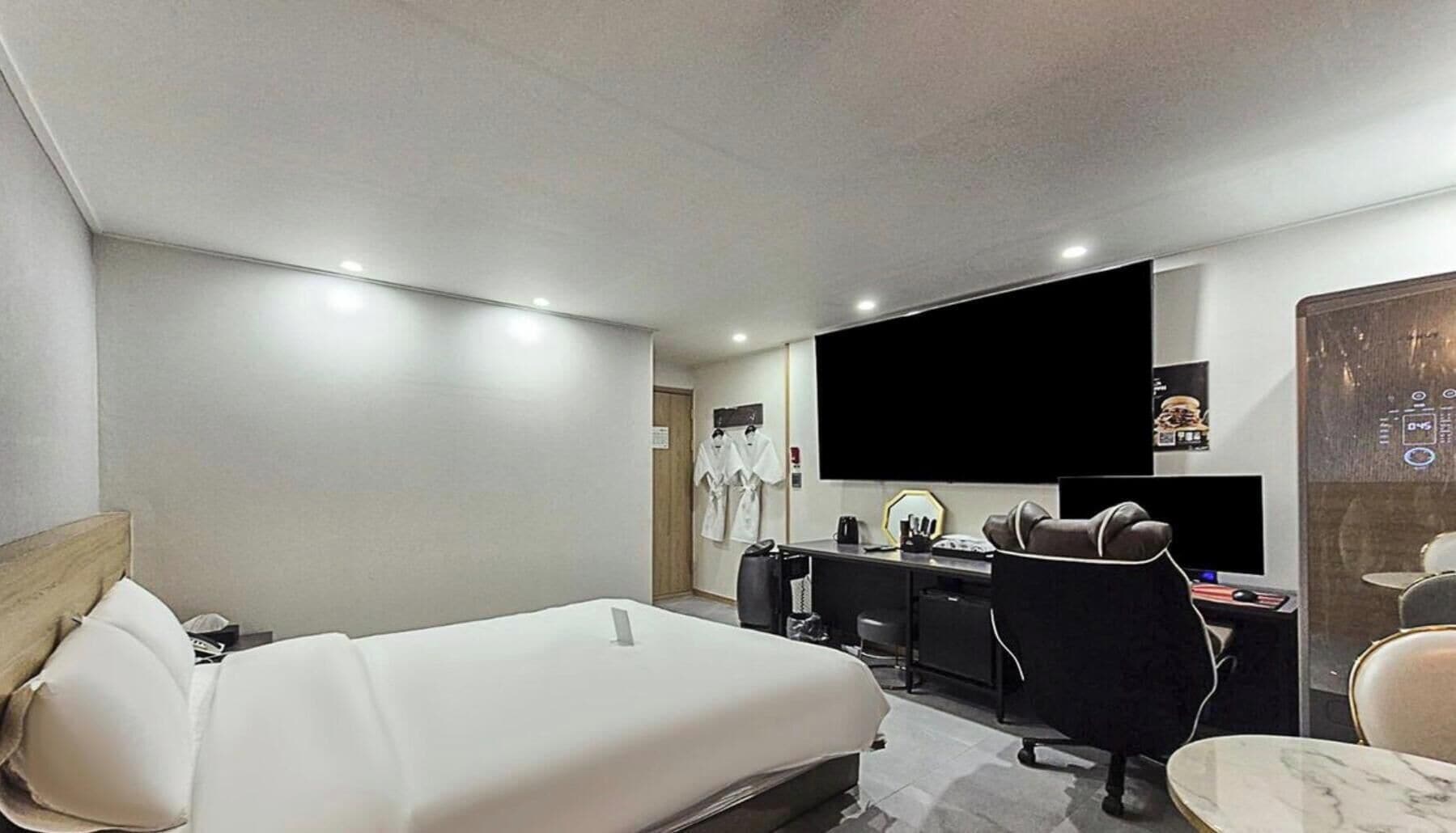 A hotel room with a bed, desk, chair, and a large flat-screen TV.