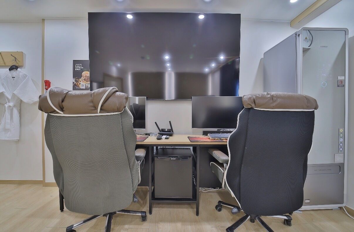 Una sala conferenze con due sedie da ufficio, una scrivania con un computer, una televisione a schermo piatto e un piccolo armadietto.