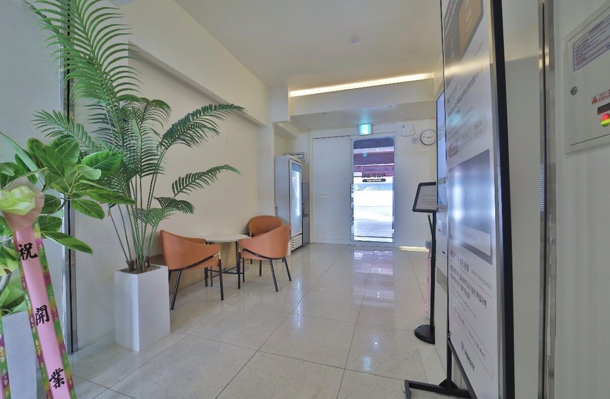 Un vestíbulo de hotel con mostrador de recepción, zona de estar, plantas en macetas y un panel informativo en la pared.
