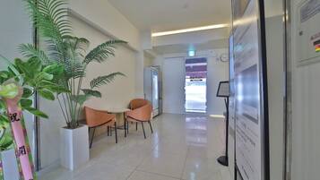 Un vestíbulo de hotel con mostrador de recepción, zona de estar, plantas en macetas y un panel informativo en la pared.