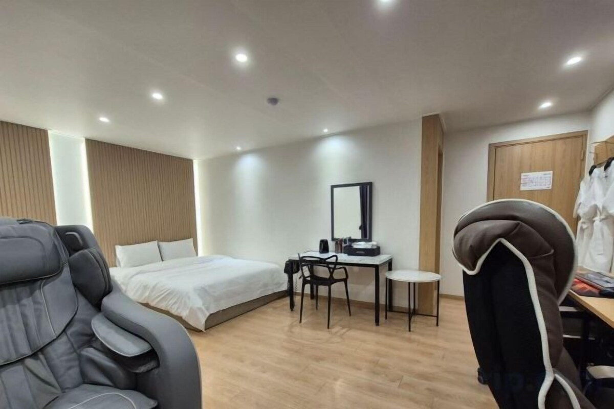 A hotel room with a bed, desk, chair, massage chair, and a wardrobe.