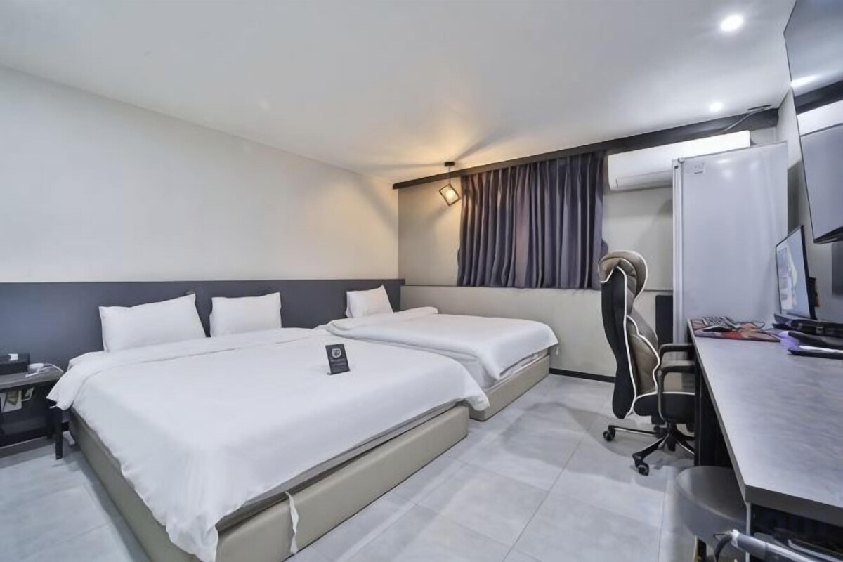 A hotel room with two beds, a desk with a computer, and a chair.