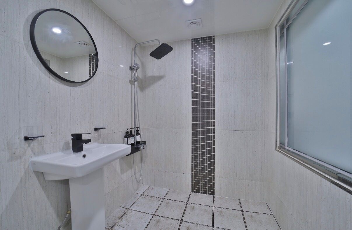 A bathroom with a white sink, a mirror, a shower, and tiled walls.