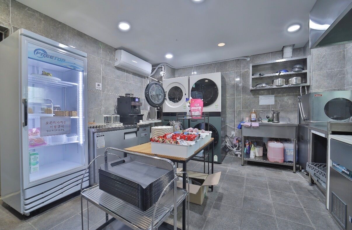 A kitchen with a refrigerator, washing machines, and a table with food items.