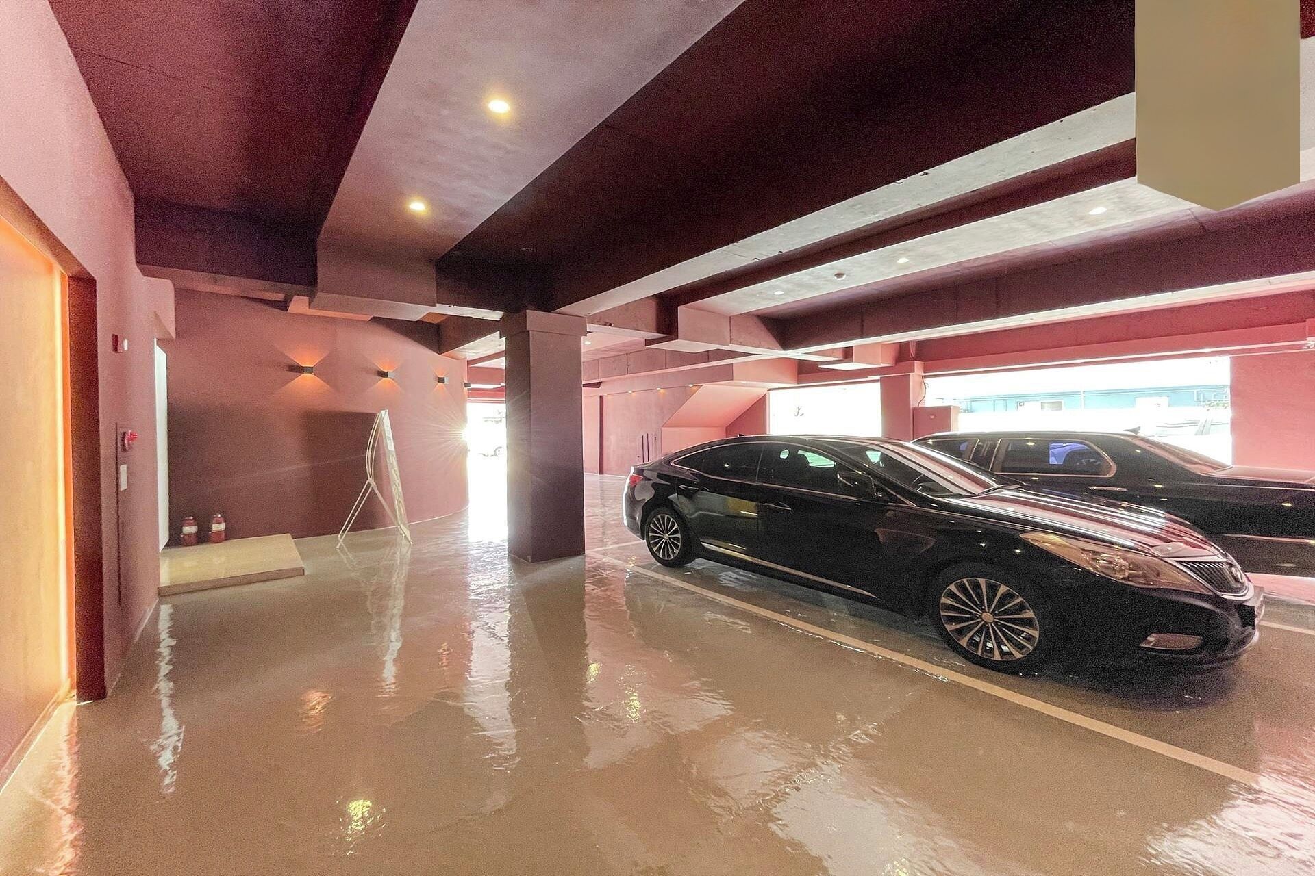 A parking garage with a wet floor, a black car, and a ladder.