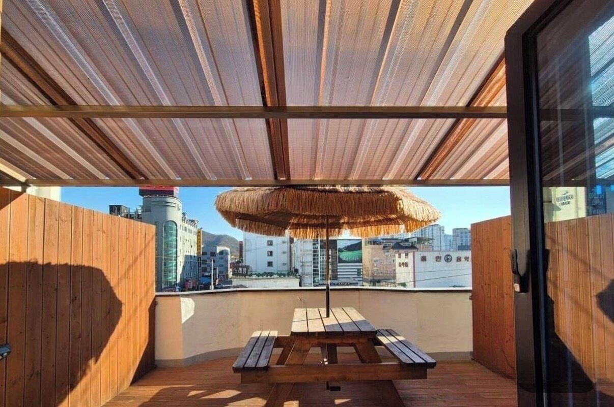 Una terraza en la azotea con una mesa y bancos de madera, un toldo de paja y vistas a la ciudad.