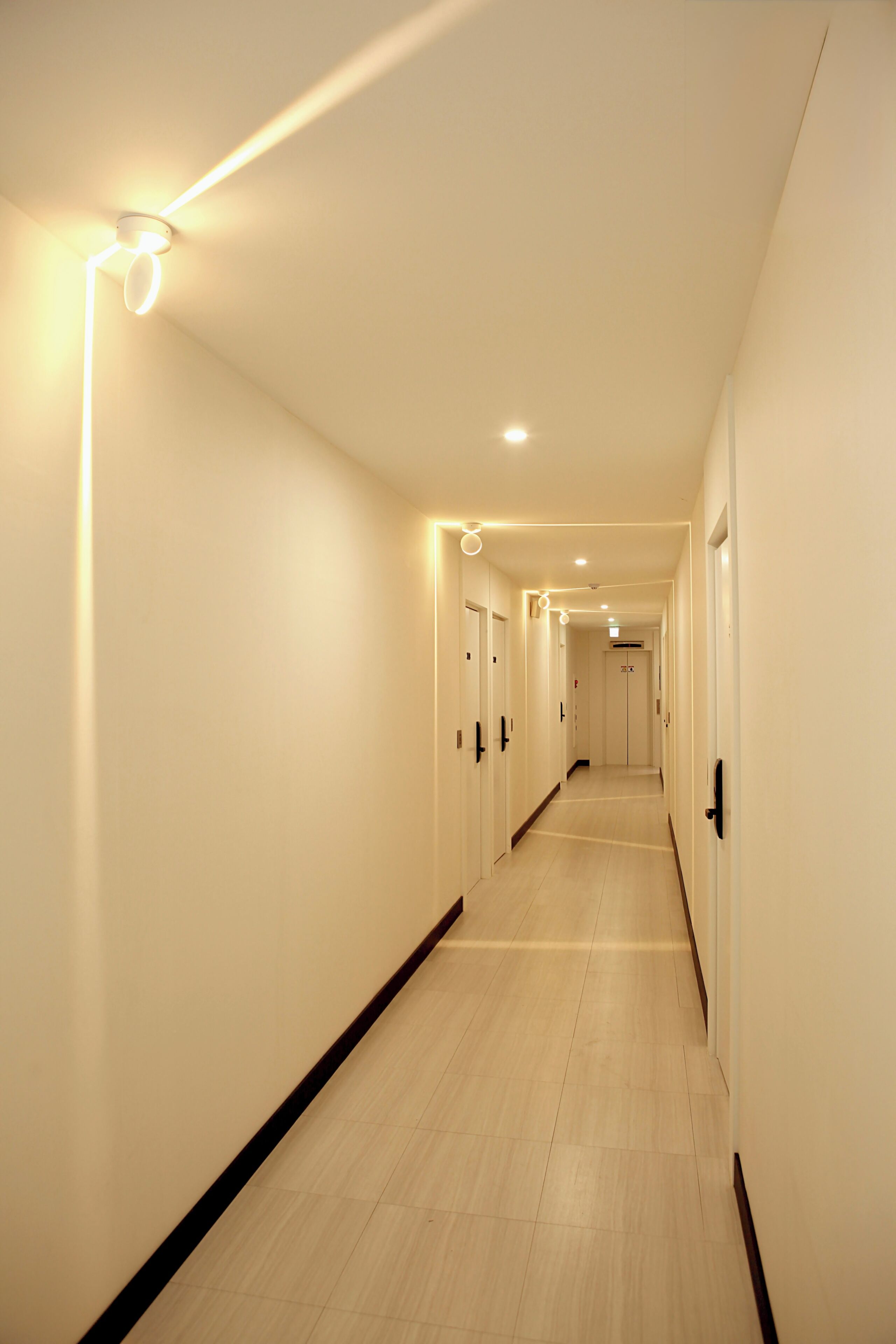 A long, narrow hallway with doors on both sides, recessed lighting, and a tiled floor.