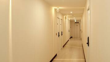 A long, narrow hallway with doors on both sides, recessed lighting, and a tiled floor.