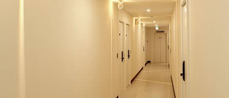 A long, narrow hallway with doors on both sides, recessed lighting, and a tiled floor.