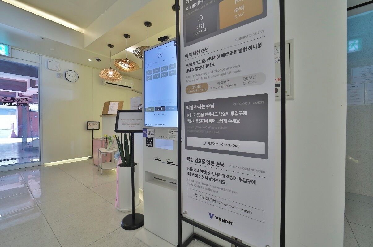 A hotel reception area with a digital display, a clock, and a VENDIT sign.