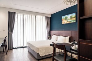 Habitación de hotel con cama, escritorio, silla, un cuadro y vistas al exterior.