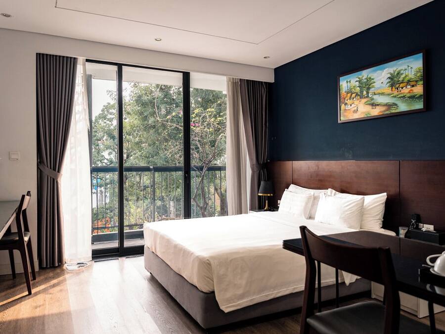 A hotel room with a bed, a desk, a chair, a nightstand, and a painting on the wall.