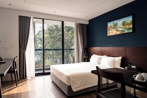 Quarto de hotel com cama, escrivaninha, cadeira, mesa de cabeceira e um quadro na parede.