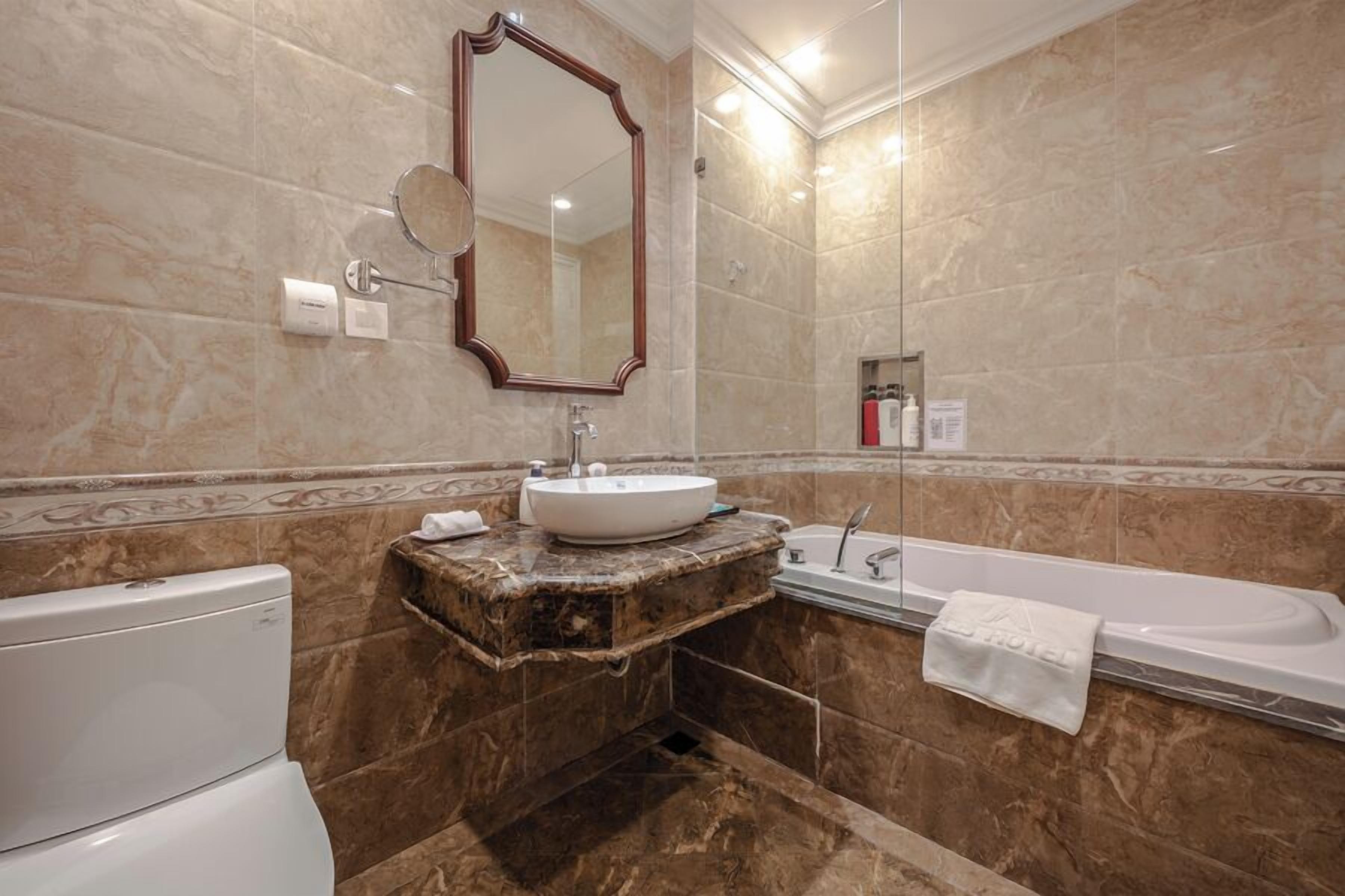 A bathroom with a marble sink, a large mirror, a bathtub, and a toilet.