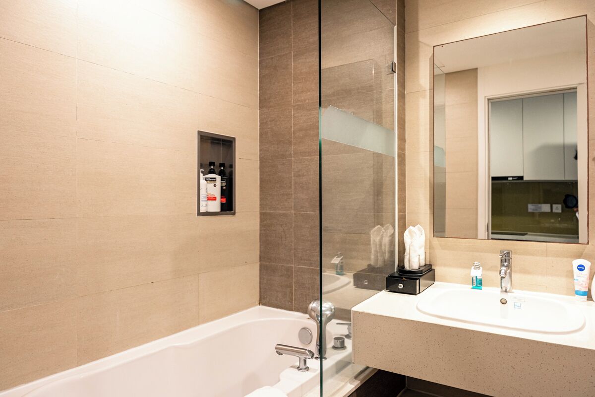 Une salle de bain moderne avec une cloison en verre, une baignoire blanche, un lavabo avec des articles de toilette et un grand miroir.