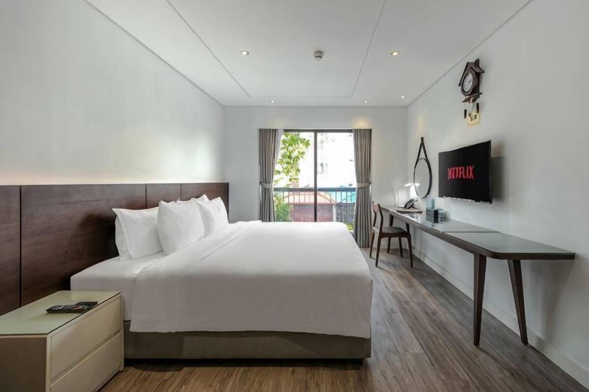A hotel room with a bed, a desk, a TV, and a window.