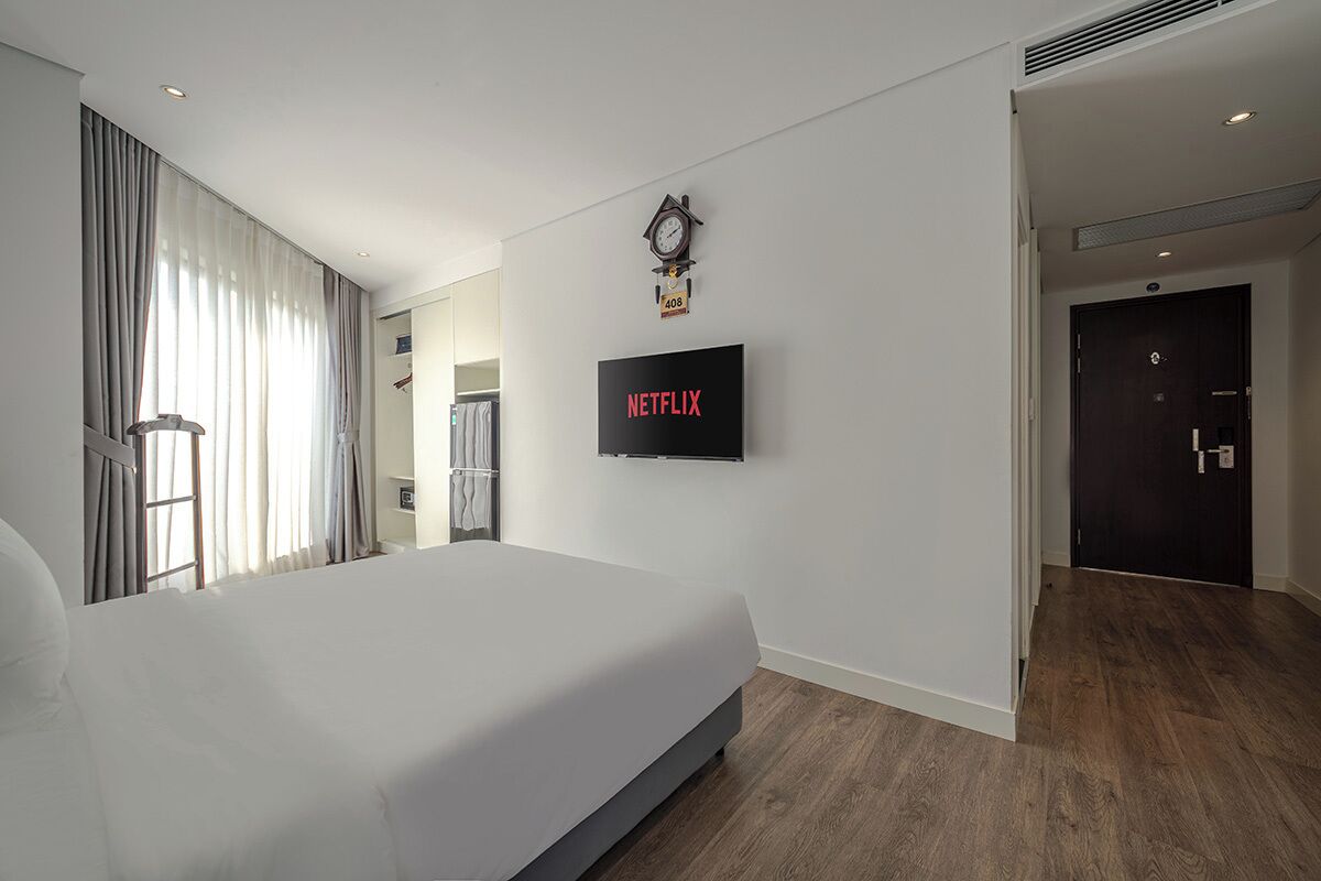A modern hotel room with a large bed, a wall-mounted TV, a clock, and a door leading to another room.
