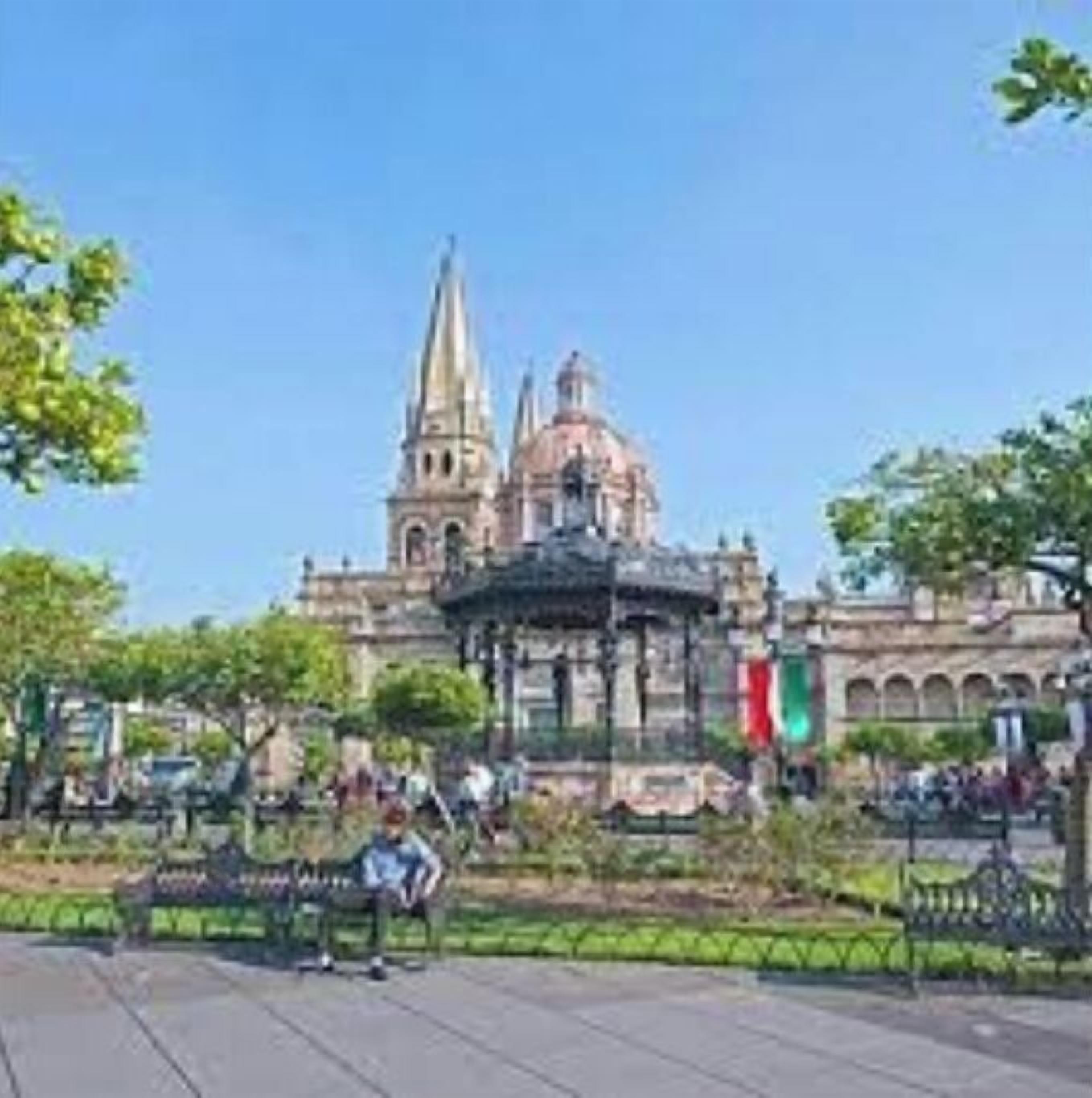 Un edificio storico con una cupola e guglie imponenti, circondato da un parco con panchine e vegetazione.