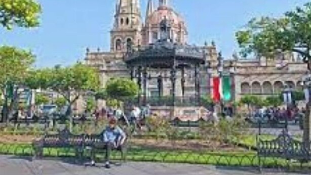 A historic building with a prominent dome and spires, surrounded by a park with benches and greenery.