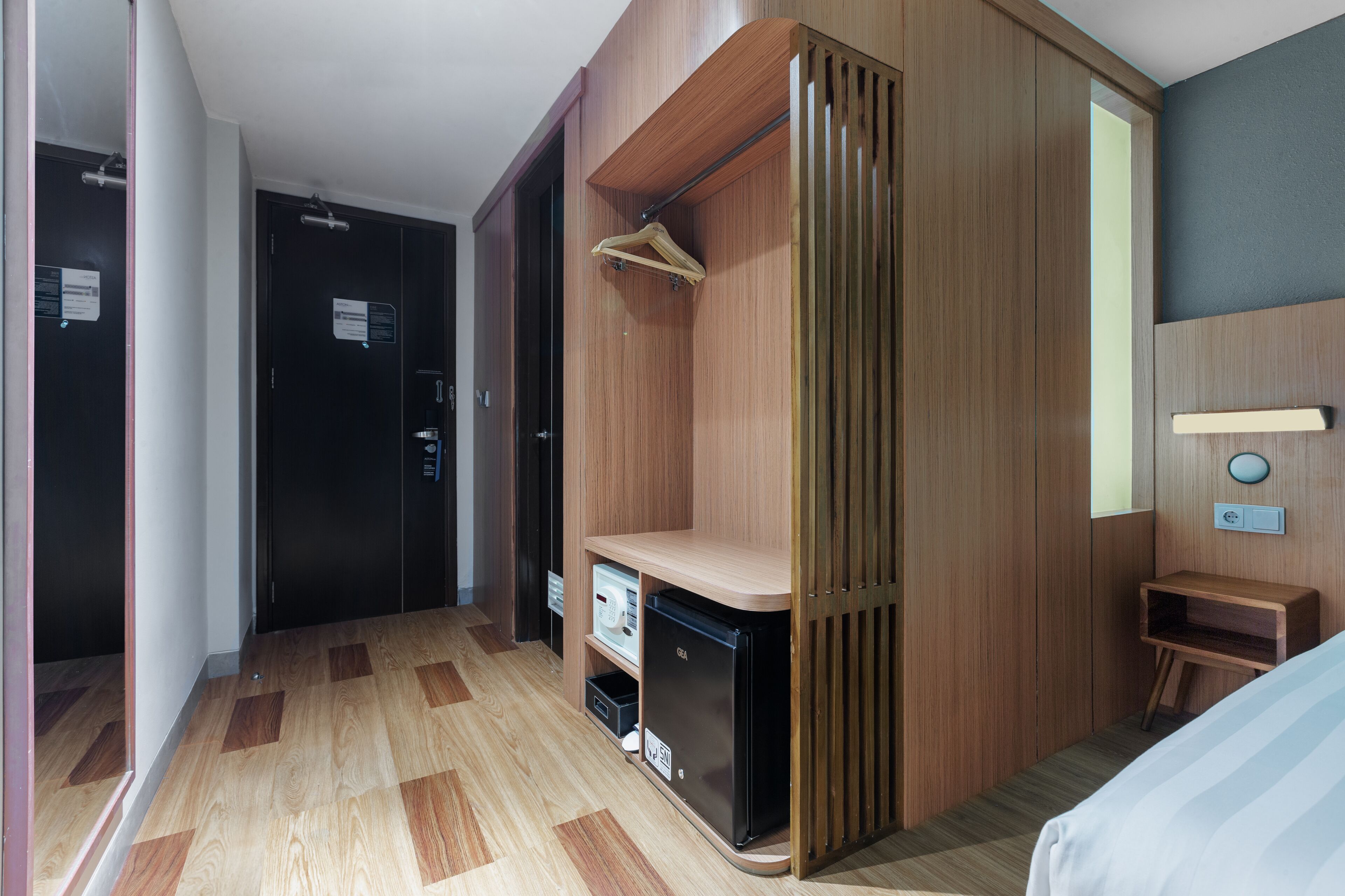 A hotel room with a wardrobe, a small desk, and a bed.