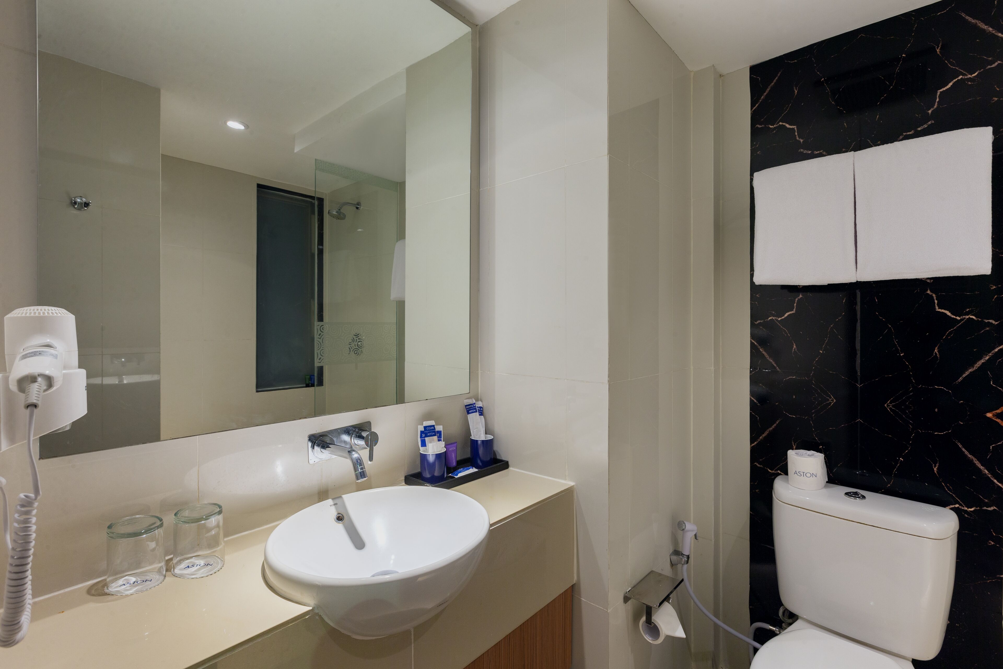 Een moderne badkamer met een wit wastafel, spiegel en een wand van zwart marmer.