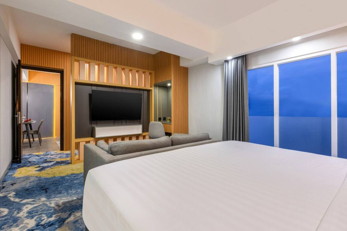 A hotel room with a large bed, a TV, a seating area with a sofa and armchairs, and a balcony with a view.