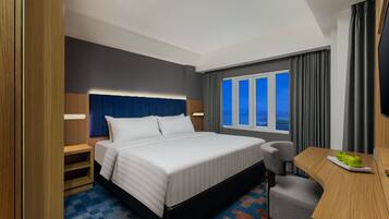 A hotel room with a bed, a desk, a chair, a window with curtains, and a view of the outside.