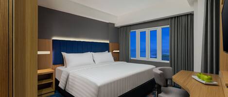 Habitación de hotel con cama, escritorio, silla, ventana con cortinas y vista al exterior.