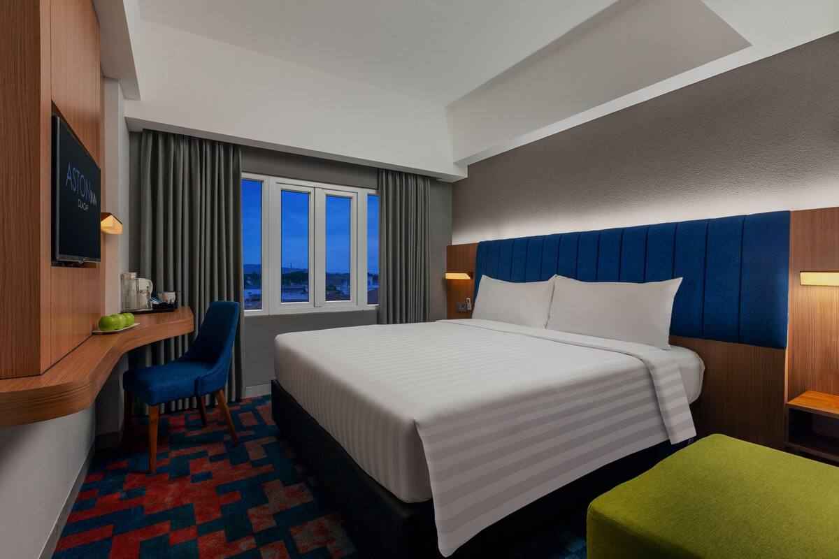 A hotel room with a bed, a desk, a chair, a TV, and a window with curtains.