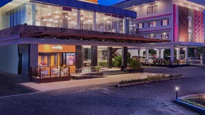 Un hotel moderno con una cafetería en la planta baja, amplios ventanales y un área de estar al aire libre techada.