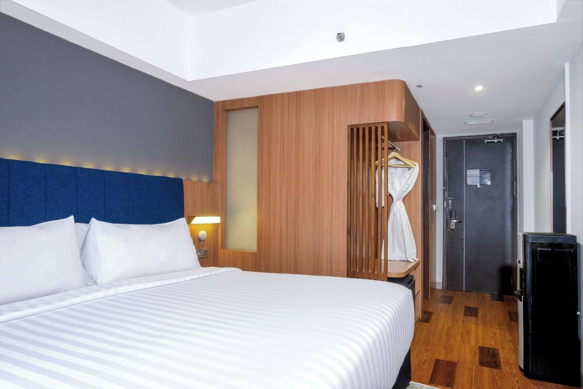 A hotel room with a large bed, a wooden panel wall, a wardrobe, and a door.