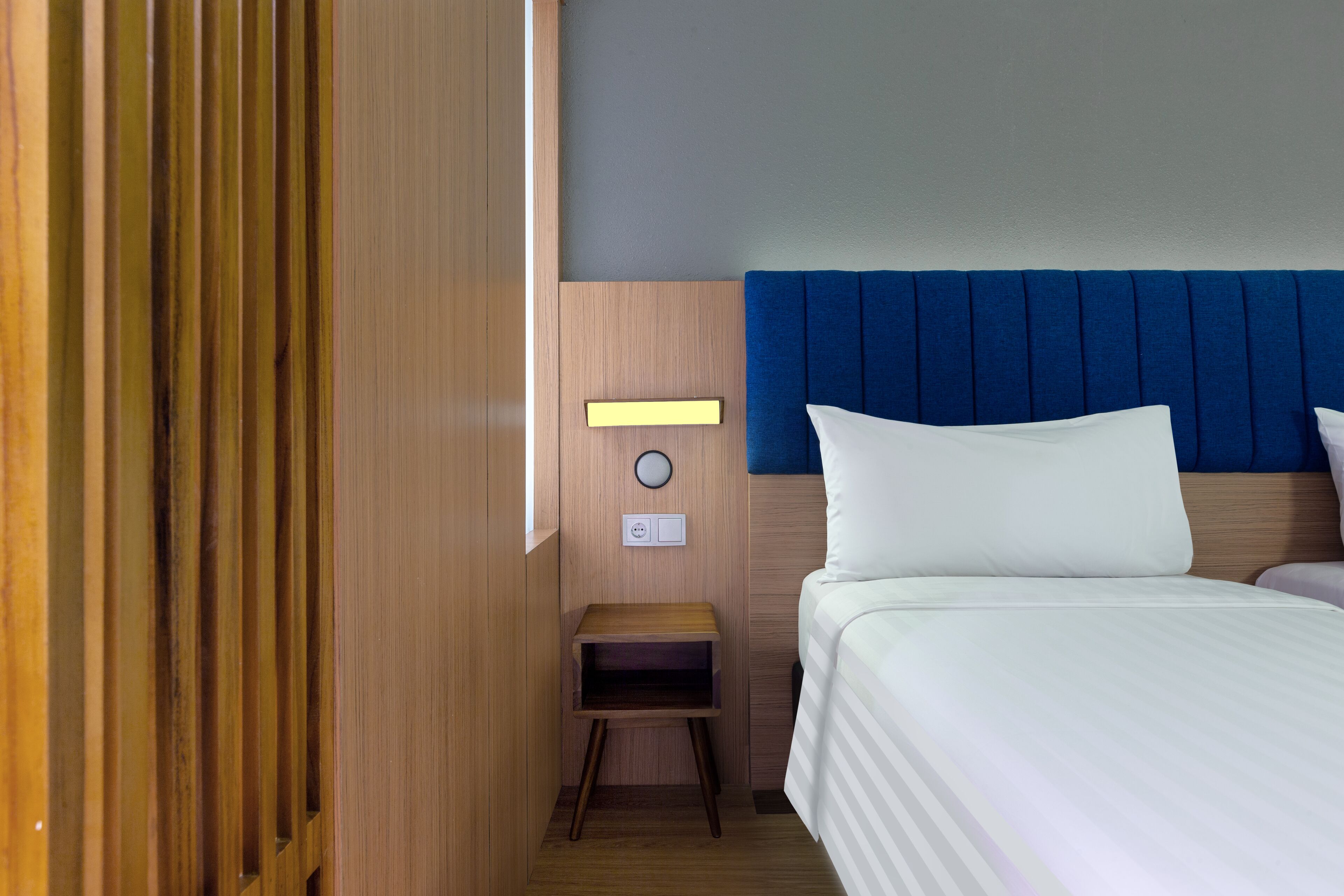Een hotelkamer met een bed, nachtkastje, een lampje aan de muur en een klein tafeltje.