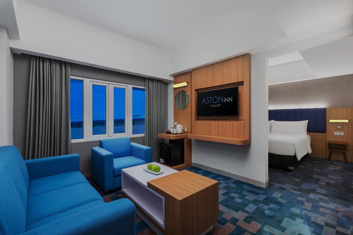 A hotel room with a large window, a flat-screen TV, a bed, a desk, and a blue sofa.