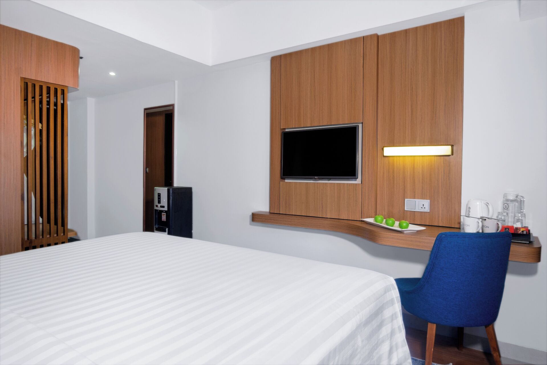 A hotel room with a bed, a desk with a flat-screen TV, a coffee maker, and a water dispenser.