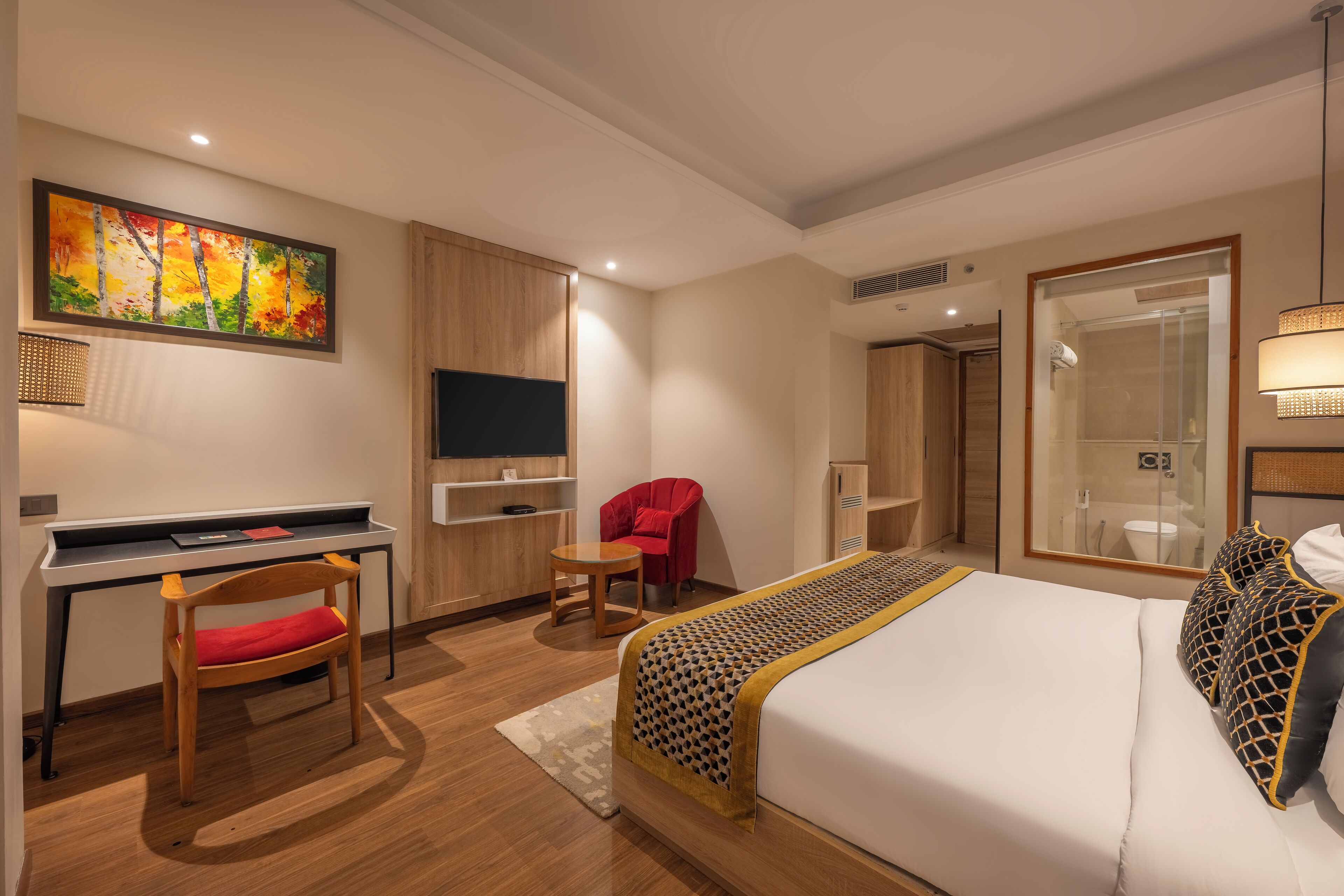 A hotel room with a bed, desk, chair, TV, and a large painting on the wall.