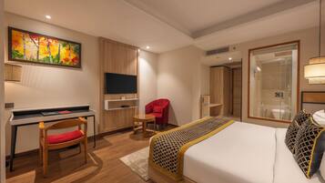 Quarto de hotel com cama, escrivaninha, cadeira, televisão e uma pintura grande na parede.
