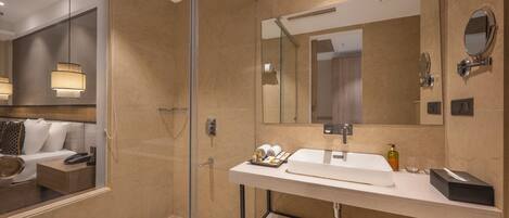 Un baño moderno con cabina de ducha de vidrio, un espejo grande y un lavamanos blanco con artículos de aseo.