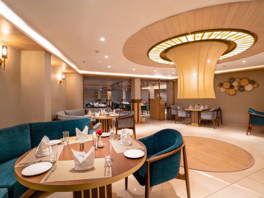 Een moderne eetruimte met ronde tafels, blauwe fauteuils en een centraal hanglamp.